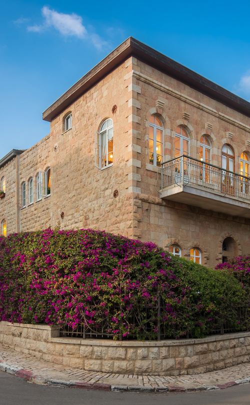 A Jerusalem stone house with arched windows, a balcony and bougainvillea